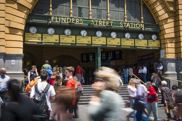 7 clocks above the entrance to flinders street station, with a blurred crowd of passersby walking in, out and in front of the entrance