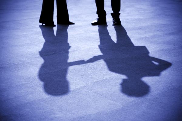 two peoples feet, with their shadows showing that they are shaking hands outside of the pictures frame