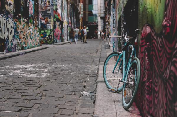 A blue bycycle leaning against a wall, as a group of people, out of focus, walk down a heavily graffitied laneway in Melbournes sidestreets