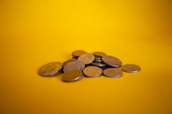A pile of various coins in Australian currency against a bright yellow bacground. Photo by Miles Burke on Unsplash