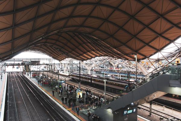 The curved roof of Southern Cross Station, with a small crowd waiting for the next train. Photo by Nao Takabayashi on Unsplash